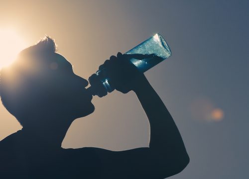 Photo of a man outside in the sun drinking from a water bottle