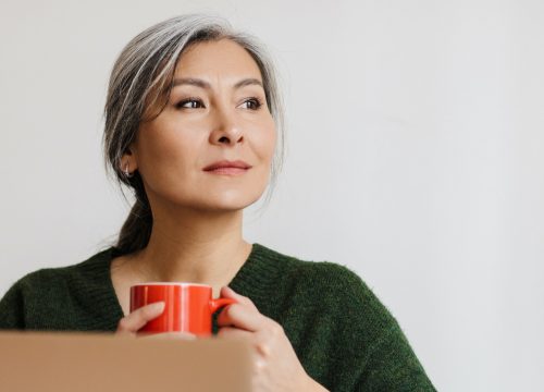 Photo of a woman working on a laptop and holding a cup of coffee