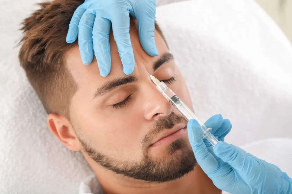 Gloved hands holding a syringe near a man’s forehead while he lies on a treatment bed
