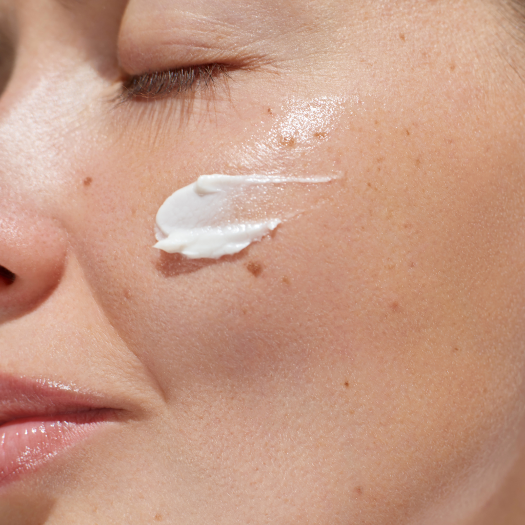 Cream applied to cheek near eye with visible freckles and skin texture