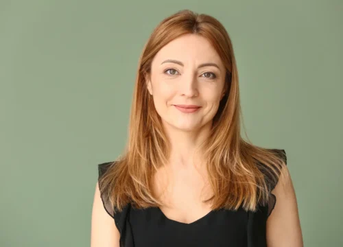 woman with shoulder-length hair wearing a black top against a green background
