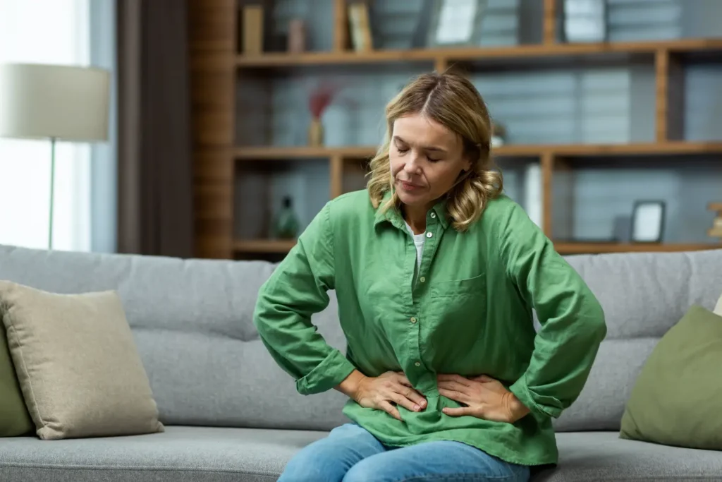 woman sitting on a couch holding her abdomen with both hands