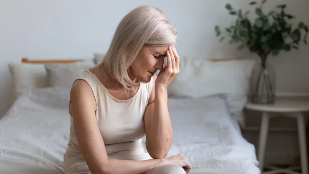 woman sitting on a bed holding her forehead with one hand