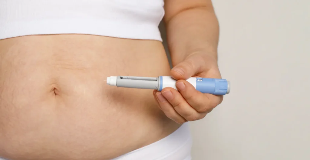 Hand holding an injection pen near the abdomen for a subcutaneous injection