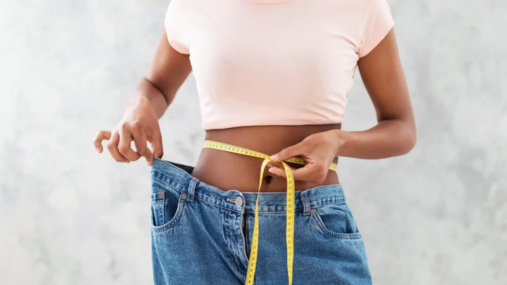 Person measuring waist with tape while holding loose-fitting jeans