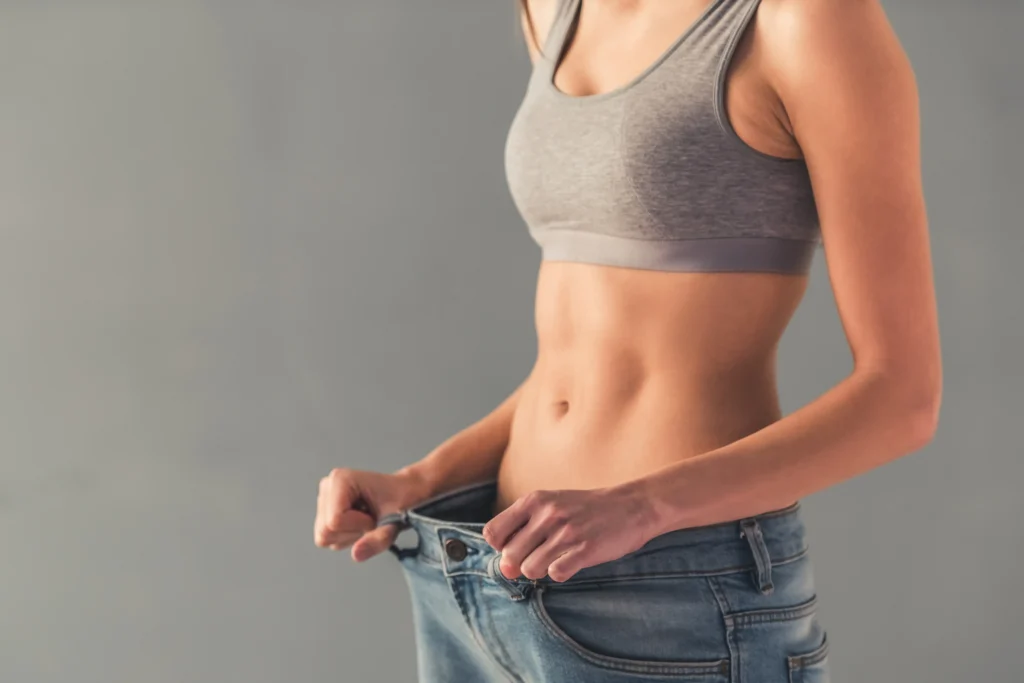 Woman pulling waistband of loose jeans to show slimmer waist
