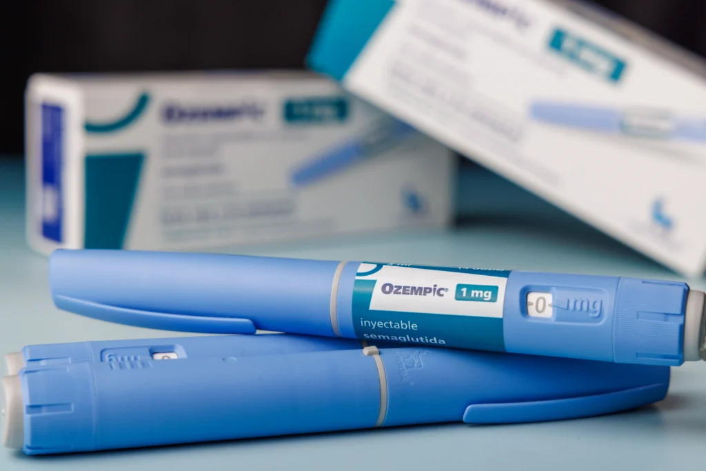 Blue injection pens labeled medication placed on surface with boxes behind