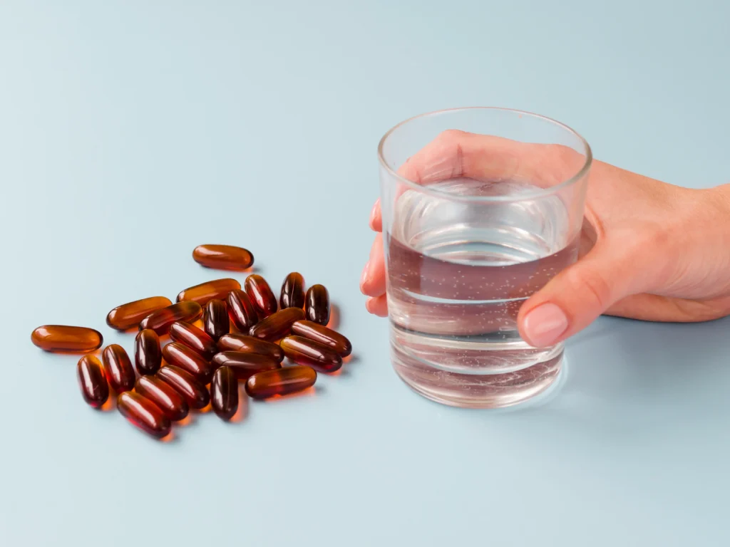 Hand holding glass of water beside brown iron supplement capsules