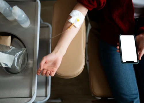 Person seated with IV infusion attached to arm while holding phone