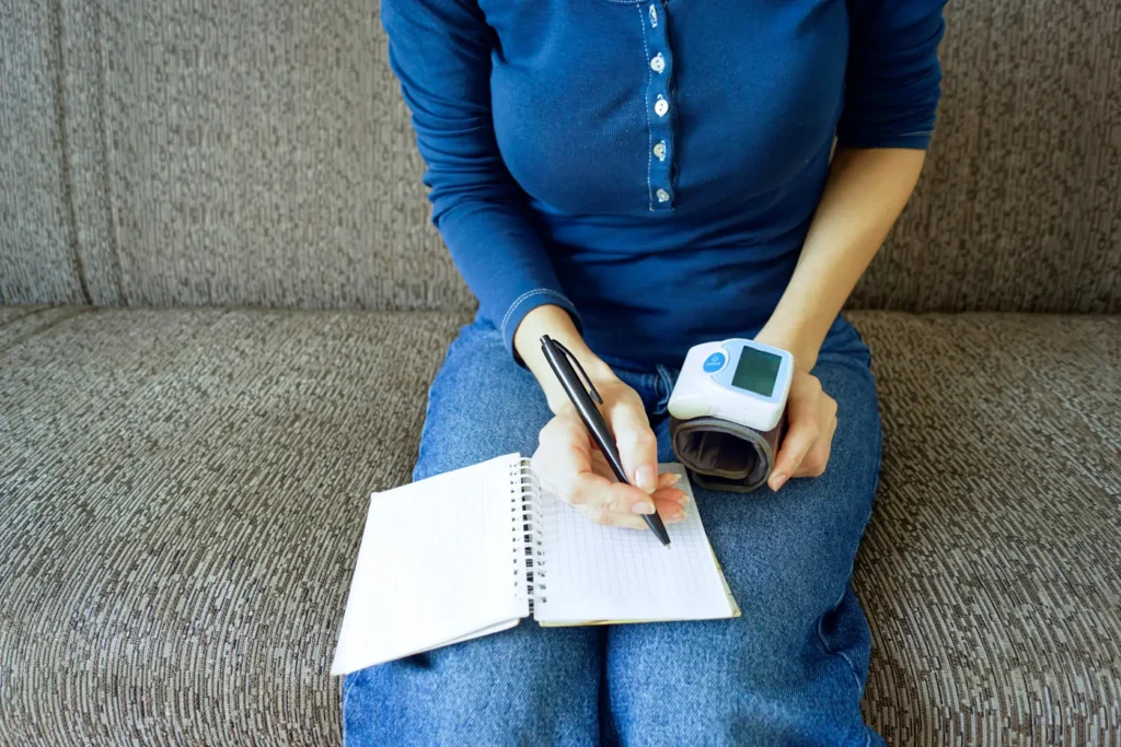 Woman writing notes while holding a digital blood pressure monitor
