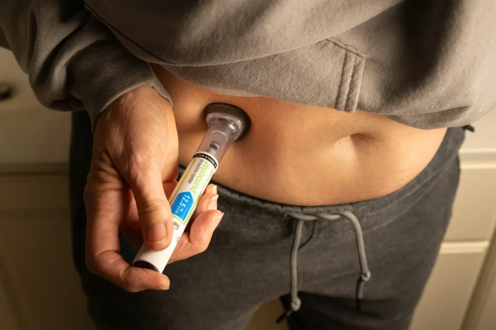 Person administering an abdominal injection while wearing a gray sweatshirt.