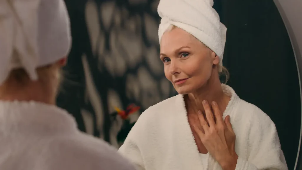 Woman in a robe and towel looking at her reflection in a mirror.