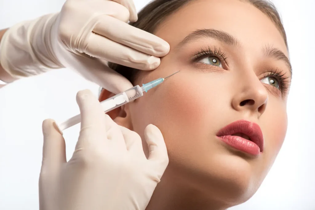 Gloved hands hold a syringe near a woman's outer eye area against a white background.