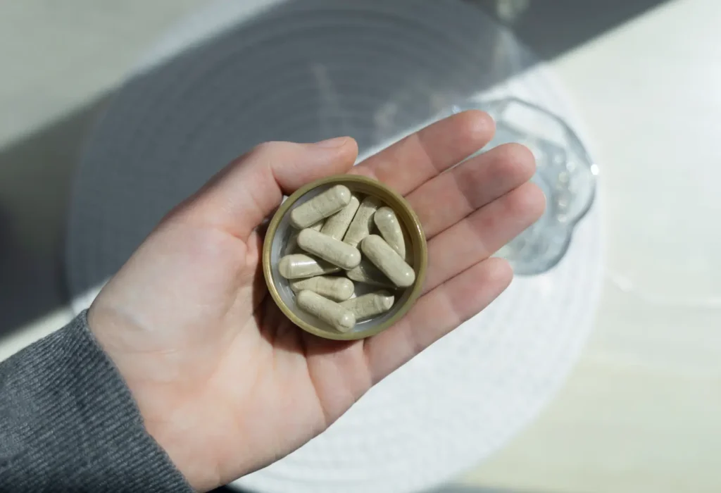 Hand holding an open container of pale capsules.
