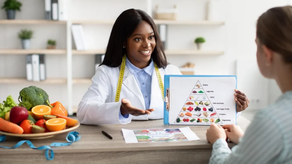 Nutrition professional discusses a food chart with a woman seated across a table with fresh produce.